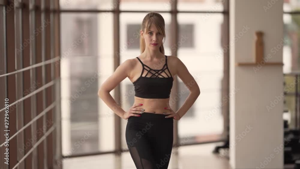 Young Caucasian Female in Leggings Warming Up Her Legs While Standing By Windows In Fitness Gym. Light Camera Movement 4k Young Caucasian Female in Leggings Warming Up Her Legs While Standing By Windows In Fitness Gym. Light Camera Movement 4k
