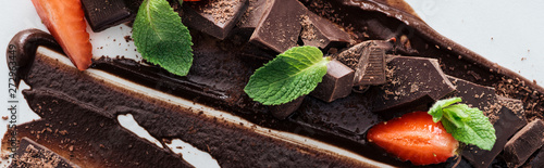 Panoramic shot of pieces of chocolate with fresh mint and strawberries