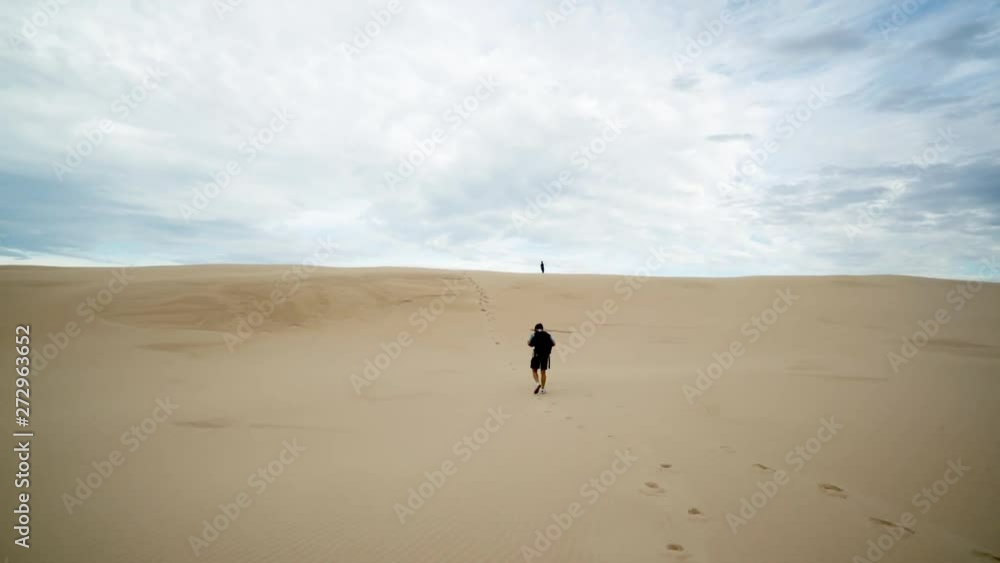 Cinematic Shot of Young Male Hiking in Desert Sand Over Dunes With Backpack Under Beautiful Australian Skyline. Camera Back Follow Movement 4k