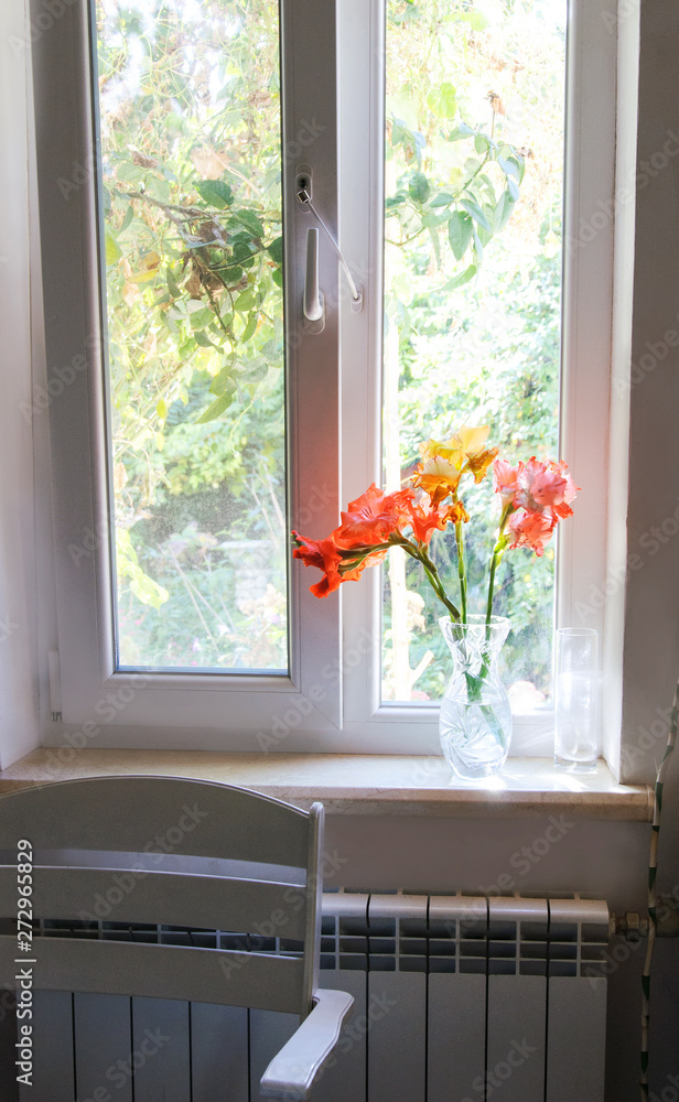 Vase with beautiful flowers on the window sill at the window in the house Vase with beautiful flowers on the window sill at the window in the house