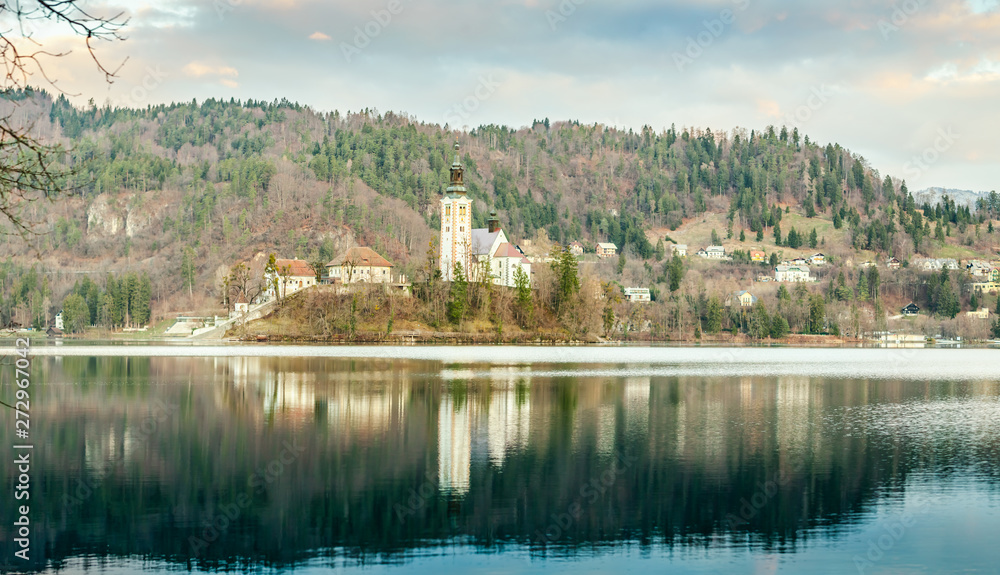 Beautiful view of famous Bled Island (Blejski otok) at scenic Lake Bled with Bled Castle (Blejski grad) and Julian Alps in the background in golden morning light at sunrise in April, 2019. Slovenia. 