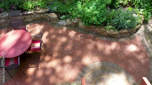 Aerial dolly motion to the left looking straight down onto finished hardscape patio with rockscaping, brickscaping and gardens melting into forest. photo