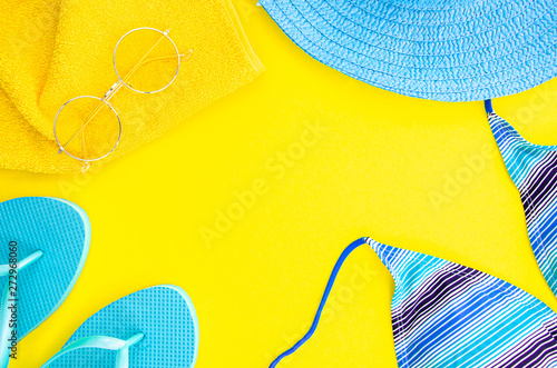 Summer flat lay mockup. Blue flip flops, palm leaf and cloth with sunglasses on yellow background. Women's blue hat and bikini. Top view frame with copy space for text or lettering