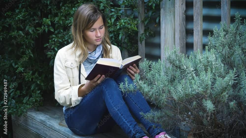 attractive teenage girl reads book in the patio among plants