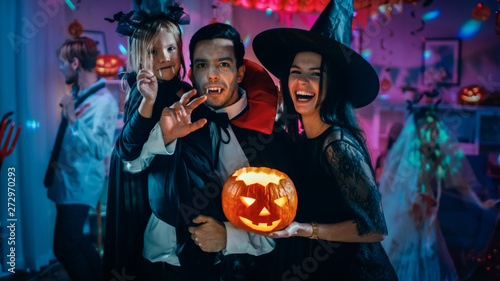 Halloween Costume Party: Father Count Dracula Holds Little Bat Girl Daughter and Hugs Witch Wife for a Happy Family Portrait. In the Background Monsters Having Fun