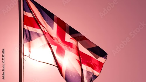 British Flag at Sunset. The Big State Flag is illuminated by the sun and flutters epically in the wind against the rising sun. Slow Motion 240 fps photo