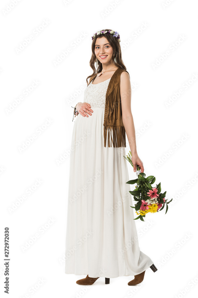 full length view of pregnant hippie woman in wreath holding flowers and touching belly isolated on white