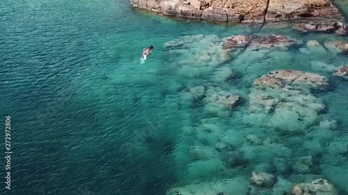 High quality drone flies over looking down at hersland ocean swimming and Snorkeling beautiful Millennial girl on vacation swims over fish in biniki filming fish and reef with action camera photo