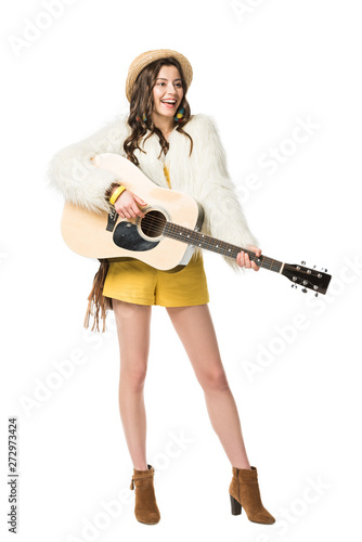 full length view of excited boho girl in straw hat playing acoustic guitar isolated on white