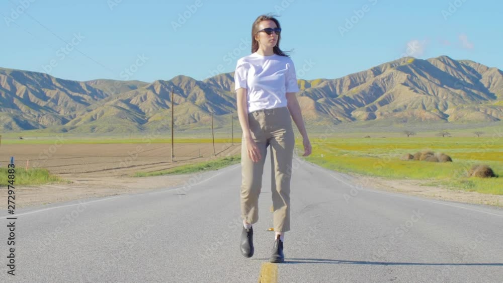 middle shot of girl walking on the straight highway with hills on the foreground middle shot of girl walking on the straight highway with hills on the foreground