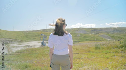 shot of girl standing next to the barwire fance with oil pumpjack on the background photo