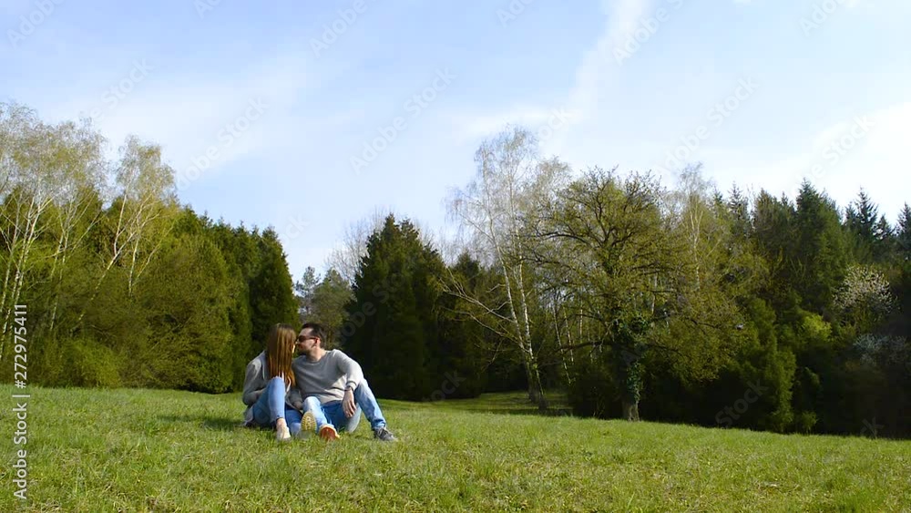 Young couple sitting on the grass in a public park, kissing and enjoying a beautiful sunny day Young couple sitting on the grass in a public park, kissing and enjoying a beautiful sunny day