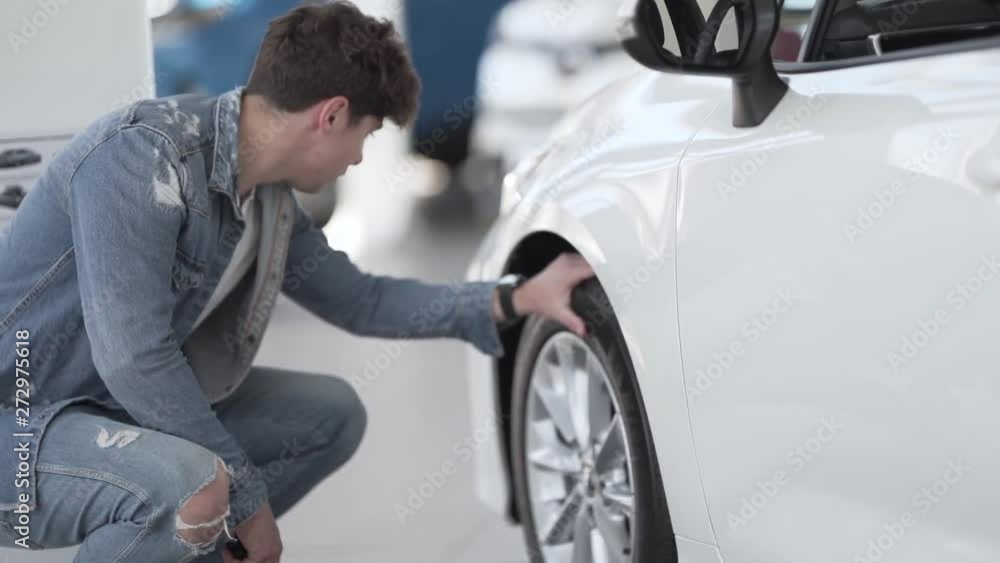 Young handsome man is choosing a car to buy. He is looking on the white one. Young handsome man is choosing a car to buy. He is looking on the white one.