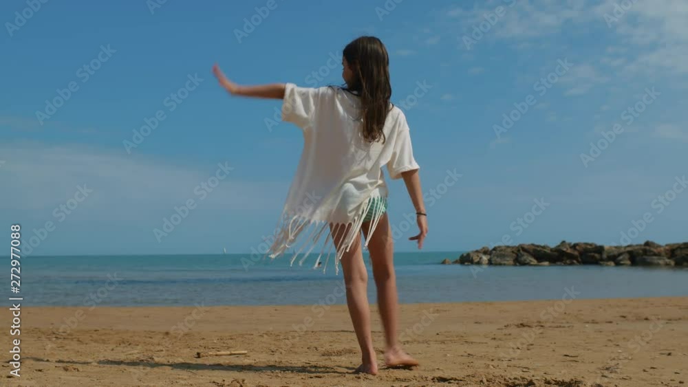 A beautiful young girl at the beach on a sunny day, dancing on the sand with the sea in the background. STATIC SHOT. A beautiful young girl at the beach on a sunny day, dancing on the sand with the sea in the background. STATIC SHOT.