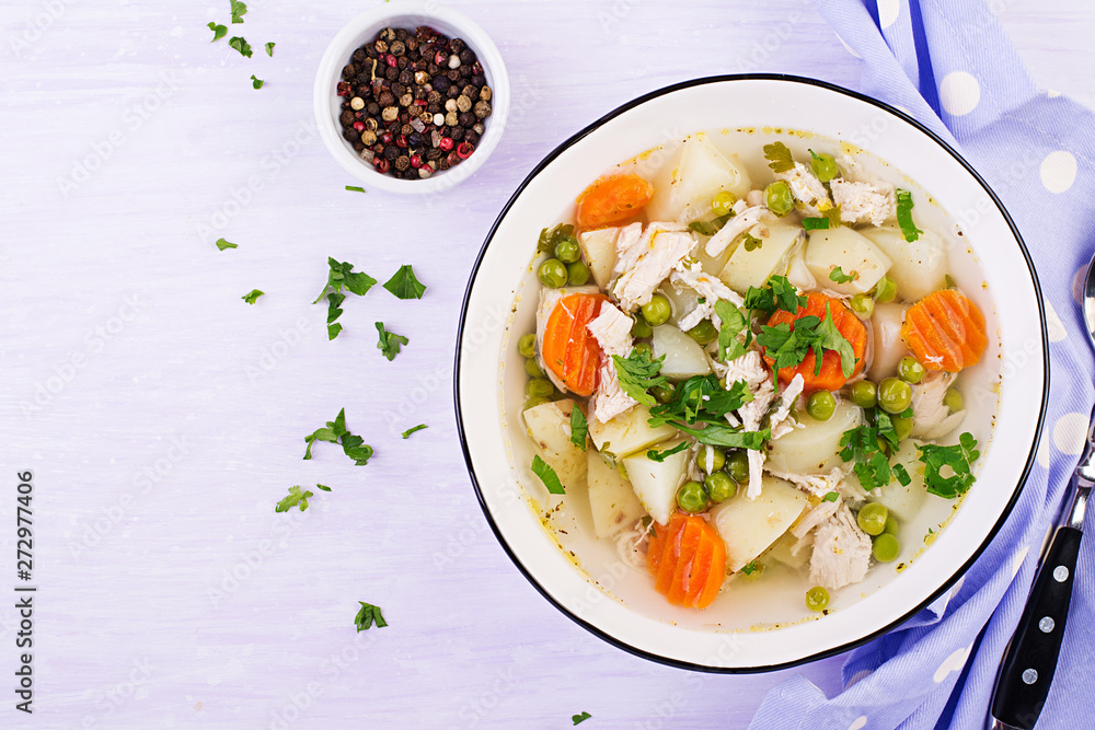 Chicken soup with green peas, carrots and potatoes in a white bowl on a light background. Top view Chicken soup with green peas, carrots and potatoes in a white bowl on a light background. Top view