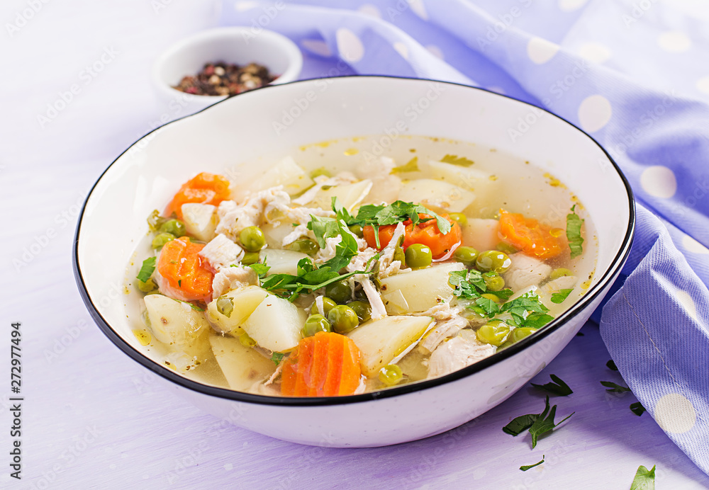 Chicken soup with green peas, carrots and potatoes in a white bowl on a light background. Chicken soup with green peas, carrots and potatoes in a white bowl on a light background.