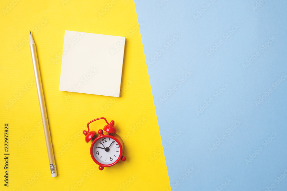 Stickers stationery and a clock on a yellow blue table with a copy of space. Concept school education, office and freelancing. Stickers stationery and a clock on a yellow blue table with a copy of space. Concept school education, office and freelancing.