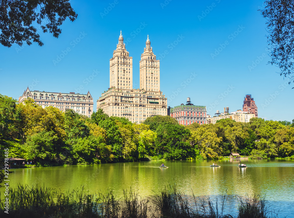 Central Park Lake and Upper West Side. Beautiful greenish colors of the forest vegetation and boat rides through the beautiful lake. View of Manhattan skyscrapers.