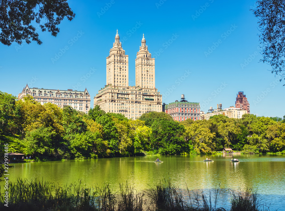 Central Park Lake and Upper West Side. Beautiful greenish colors of the forest vegetation and boat rides through the beautiful lake. View of Manhattan skyscrapers. Central Park Lake and Upper West Side. Beautiful greenish colors of the forest vegetation and boat rides through the beautiful lake. View of Manhattan skyscrapers.