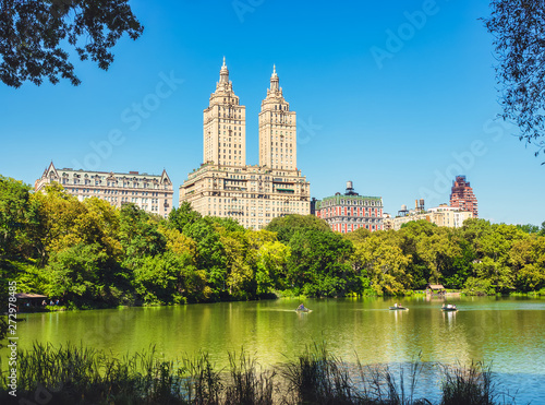 Central Park Lake and Upper West Side. Beautiful greenish colors of the forest vegetation and boat rides through the beautiful lake. View of Manhattan skyscrapers.