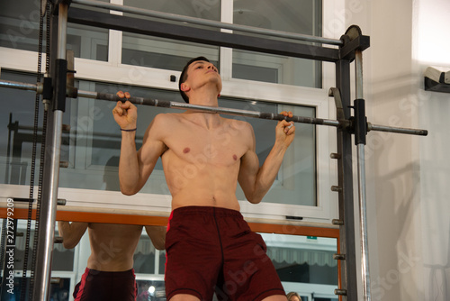 The young male exercises in the gym uses the multipower. Concept of fitness, sport, training, gym and lifestyle.