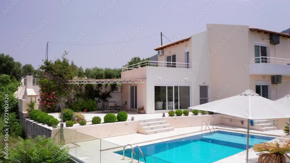 Aerial Pull Away from Luxury Greek Villa with Pool, Sun Loungers & Miniature Palm Trees on Sunny Day Aerial Pull Away from Luxury Greek Villa with Pool, Sun Loungers & Miniature Palm Trees on Sunny Day