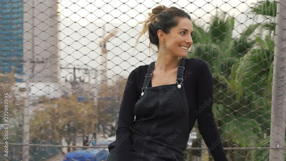 Portrait of a young beautiful woman outside in the city wearing stylish urban clothes and smiling to camera Portrait of a young beautiful woman outside in the city wearing stylish urban clothes and smiling to camera