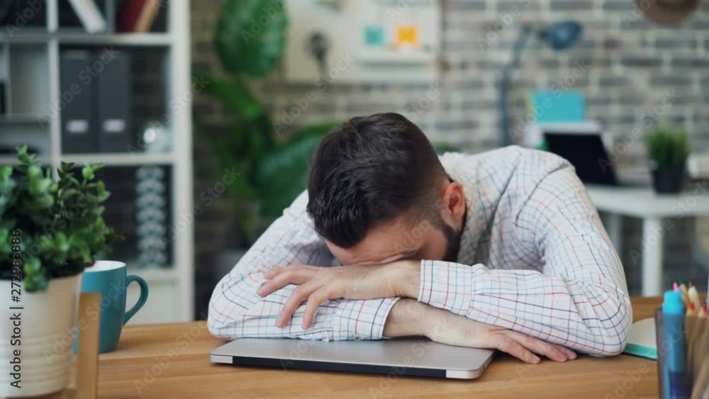 Portrait of young man tired employee sleeping on desk in office relaxing at work holding laptop computer. Overwork, lazy workers, business and youth concept. Portrait of young man tired employee sleeping on desk in office relaxing at work holding laptop computer. Overwork, lazy workers, business and youth concept.