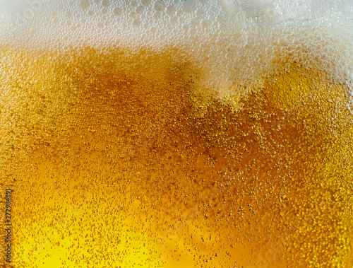 Close up view of floating bubbles in light golden colored beer background. Texture of cooling summer's filtered drink with foam and macro fizz on the glass wall. Fizzing or floating up to top of