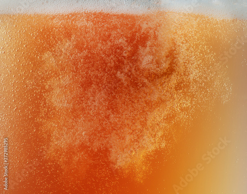 Close up view of floating bubbles in golden colored beer background. Texture of cooling summer's unfiltered drink with foam and macro fizz on the glass wall. Fizzing or floating up to top of surface.