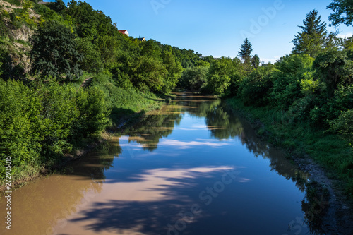 Sky  trees and shrubs are reflected in the calm waters of a small river. Summer landscape.