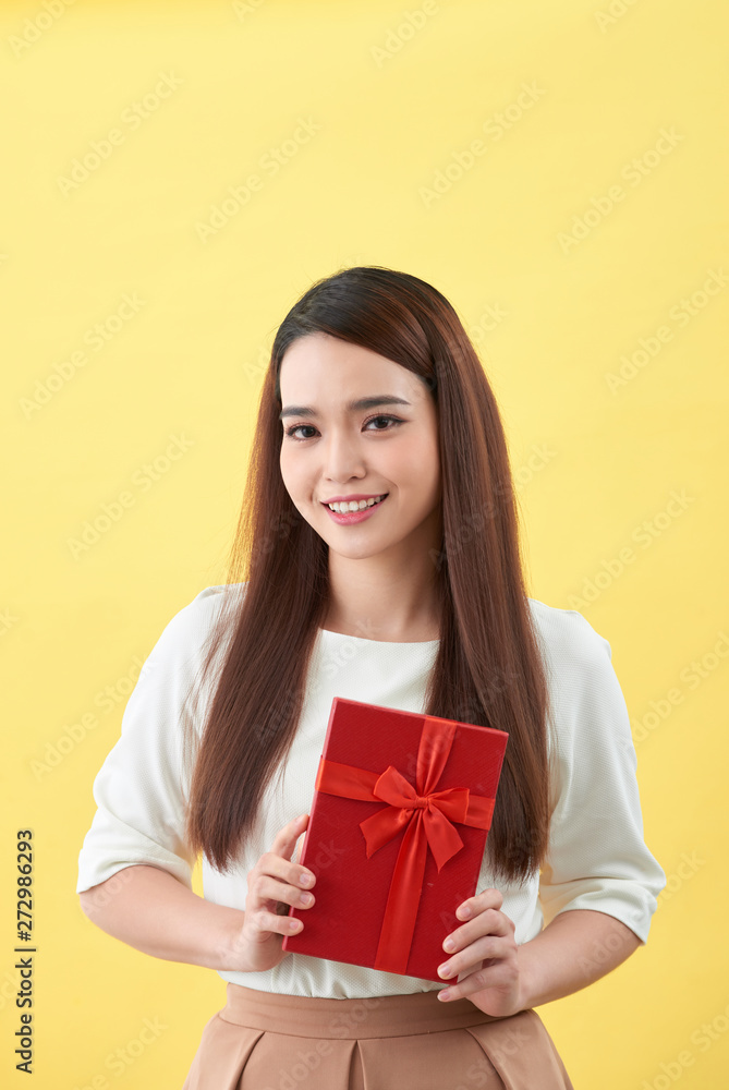 Asian woman is holding a gift box in yellow background Asian woman is holding a gift box in yellow background