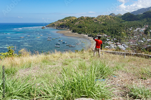 A spectacular view from the top of a hill in a remote village in Flores, East Nusa Tenggara, Indonesia. A man is watching the village and the sea from a hill