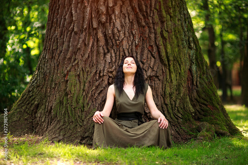 Girl in dress sits enjoying nature meditates, practices yoga in forest
