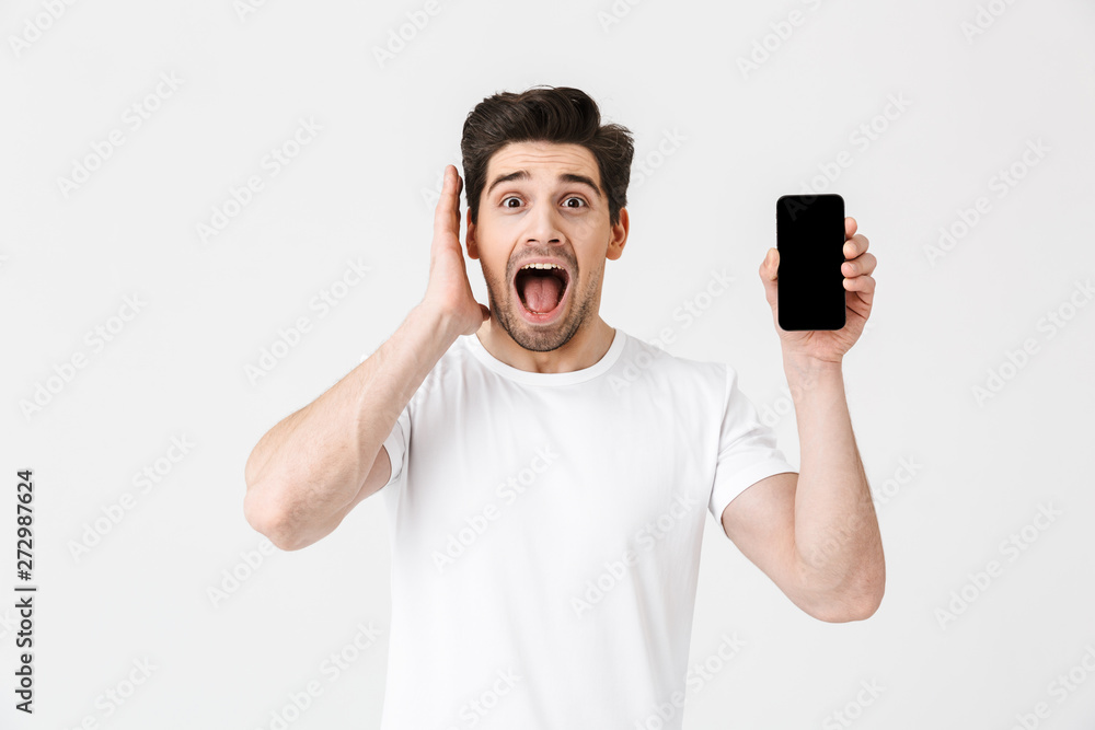 Excited happy young man posing isolated over white wall background showing display of mobile phone. Excited happy young man posing isolated over white wall background showing display of mobile phone.