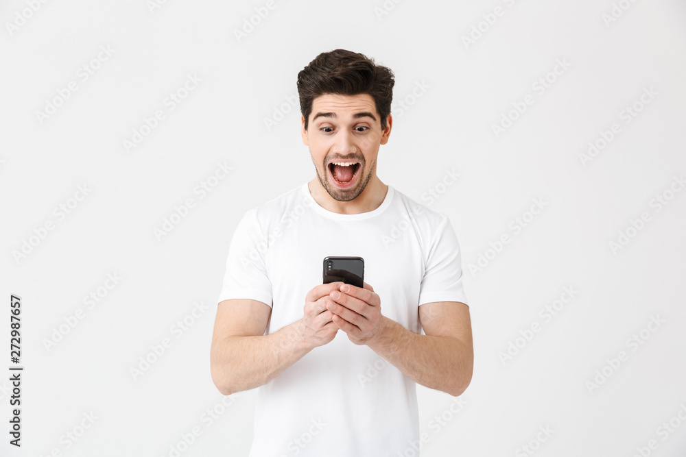 Excited happy young man posing isolated over white wall background using mobile phone. Excited happy young man posing isolated over white wall background using mobile phone.