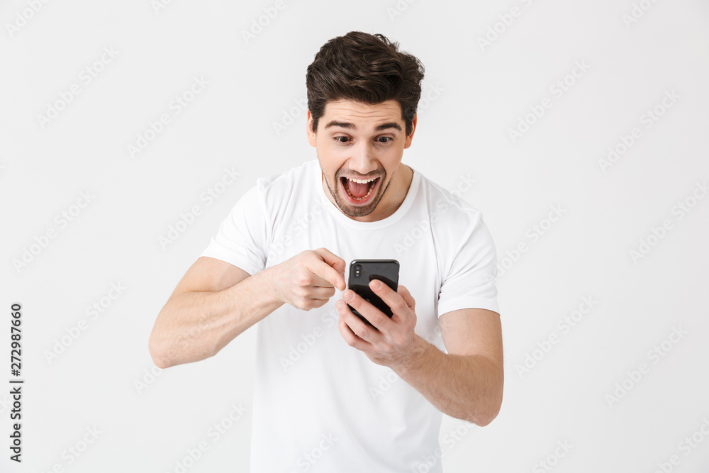 Excited happy young man posing isolated over white wall background using mobile phone. Excited happy young man posing isolated over white wall background using mobile phone.