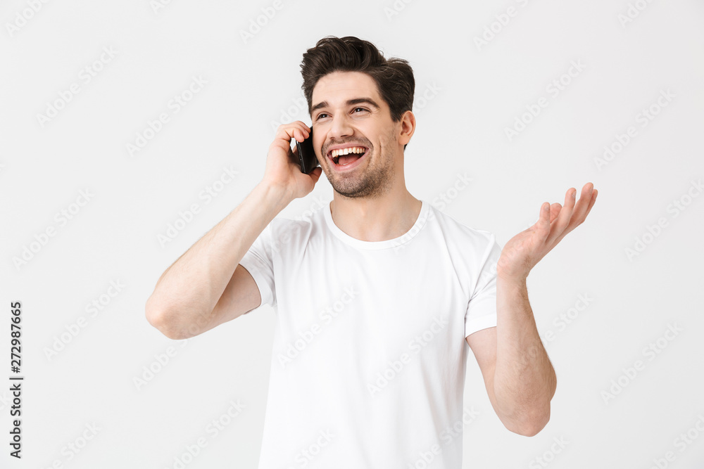 Happy young man posing isolated over white wall background talking by mobile phone. Happy young man posing isolated over white wall background talking by mobile phone.