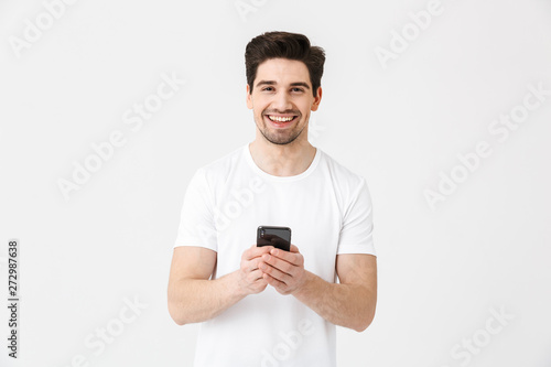 Excited happy young man posing isolated over white wall background using mobile phone. © Drobot Dean