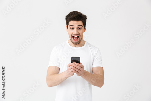 Excited happy young man posing isolated over white wall background using mobile phone.