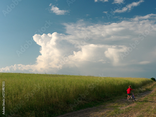 a child on a bicycle. beautiful white clouds in the sky float above the field.