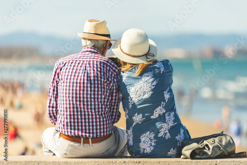 Mature couple of retired lovers enjoying retirement on the beach facing the sea with mobile cell phone taking pictures at sunset. Couple happy true love in the nature