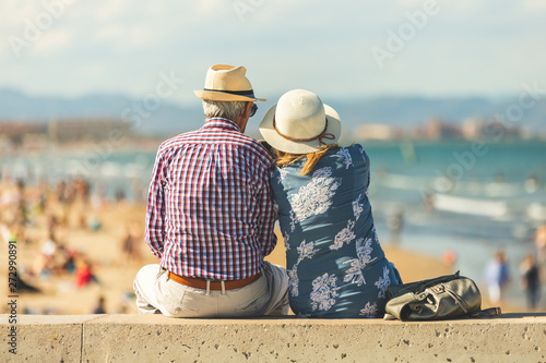 Φωτογραφία Mature couple of retired lovers enjoying retirement on the beach facing the sea with mobile cell phone taking pictures at sunset