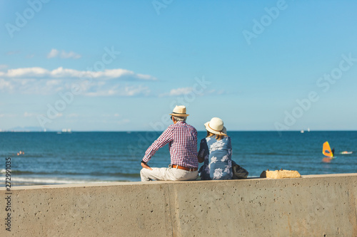 Loving the elderly couple sitting on the wall facing the beach, watching and taking pictures of the landscape on a romantic trip