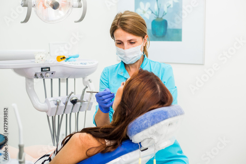 A professional dentist, a specialist, a female, inspects and checks the oral cavity of a girl’s patient, prevents caries, and performs a routine dental examination