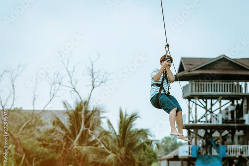 A male tourist flying on a zipline aka flying fox across the lake at Pattaya Floating Market, Thailand.