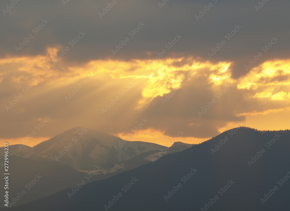 Morning landscape with mountains and orange sky at sunrise with sun reflecting. Evening sunset on the horizon of hills with snow and sun rays.