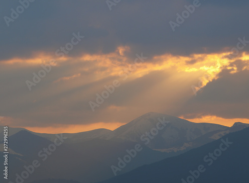 Morning landscape with mountains and orange sky at sunrise with sun reflecting. Evening sunset on the horizon of hills with snow and sun rays.