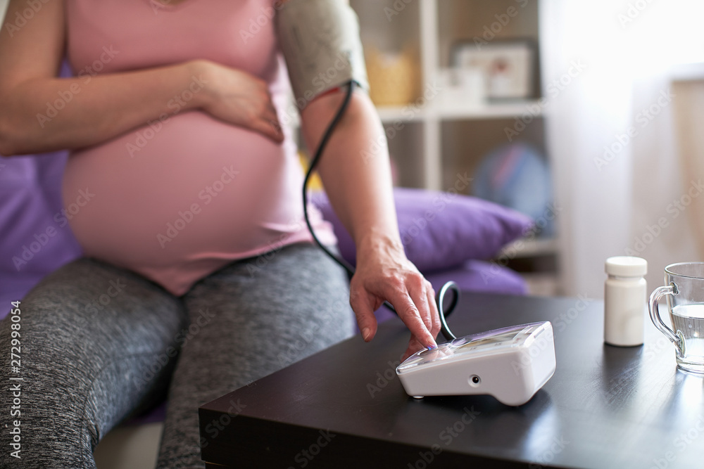 Fototapeta premium a woman measures blood pressure with an electronic pressure gauge, headache during pregnancy, poor health.