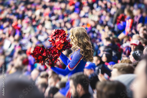 Canvas Print Female cheerleader in red blue uniform with pom-pom with audience in the backgro